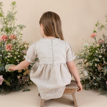 Load image into Gallery viewer, a young girl in natural colour 100% linen day dress with four buttons down back with puff sleeve. Flowers with beige background.