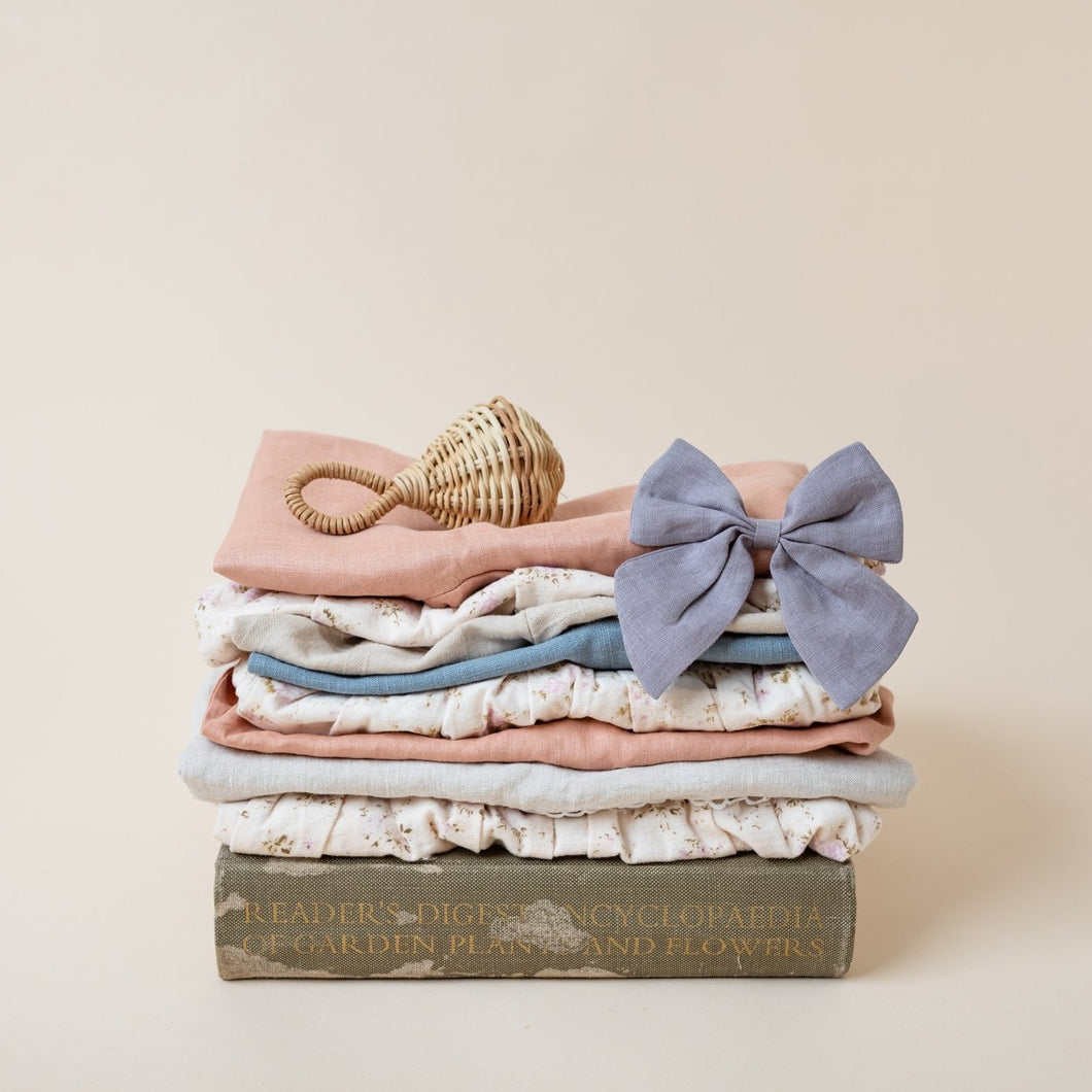 mauve linen bow on stack of linen cotton clothes flatlay with beige background